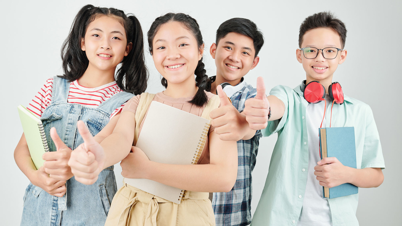 Group of happy Asian school children with books and copybooks showing thumbs-up