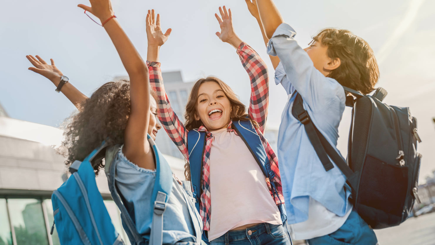 Happy children with hands up standing near school outdoors